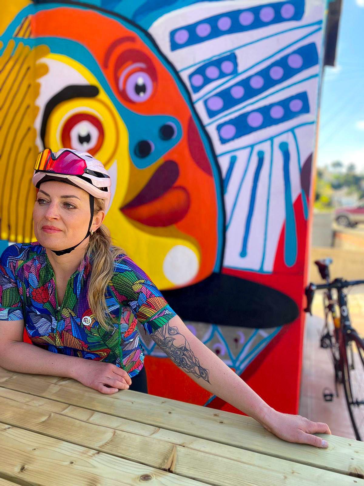 Aktywna bliźniaczka na tle kolorowej ściany w koszulce rowerowej Nessi Mosaic Paraiso